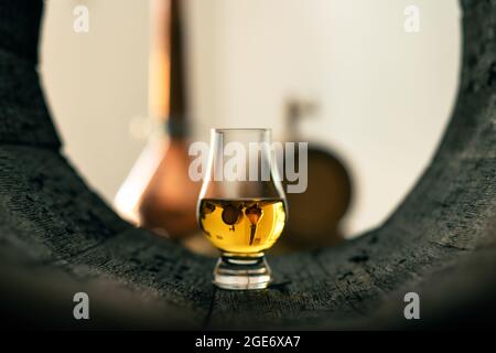 Ein Glas Whiskey im alten Eichenfass. Kupfer-Alambic auf dem Hintergrund. Traditionelles Konzept der Alkoholbrennerei Stockfoto