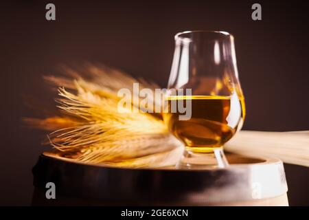 Ein Glas Whisky auf einem alten Eichenfass mit einem Strauß Roggen. Traditionelles Konzept der Alkoholbrennerei Stockfoto