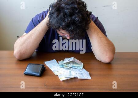 Mann mit verschiedenen Rechnungen vor ihm. Ein Mann, der seine Schulden nicht bezahlen kann. Seitenansicht. Ausdruck Stockfoto