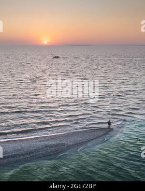 Luftaufnahme über das abendliche Meer und Spucken mit Touristen. Sonnenuntergang im Meer mit großer Sonne dämmern sanfte Wellen und leuchtend orange Himmel. Drohnenfotografie im Landschaftsbereich Stockfoto