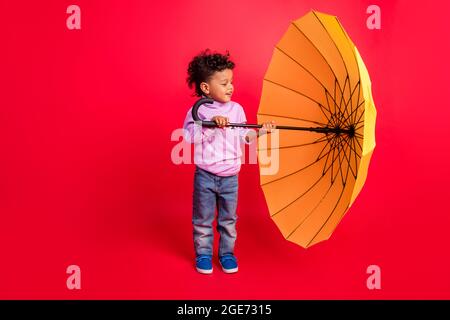In voller Länge Körpergröße Ansicht der attraktiven fröhlich preteen Kind hält Öffnung Sonnenschirm isoliert über hellen roten Hintergrund Stockfoto