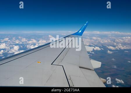 Blick vom Bullauge auf den Flugzeugflügel. Fliegen über Land und Wolken. Zum Fliegen Stockfoto