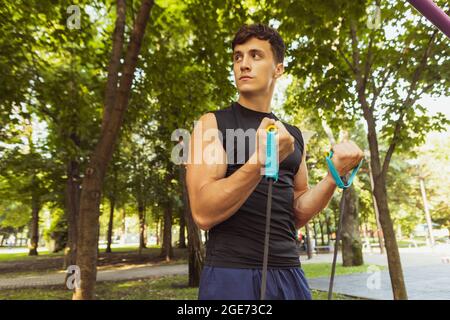 Ein junger, hübscher Kaukasusmann in Sportkleidung, der an einem hellen Sommertag mit Seil im Freien springt. Stockfoto