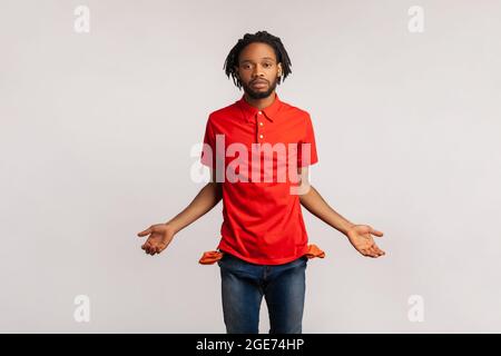 Trauriger Mann mit Dreadlocks, der ein rotes T-Shirt im lässigen Stil trägt, leere Taschen zeigt und frustriert über Kredite und Schulden aussieht, hat kein Geld, keine Arbeitslosen. I Stockfoto