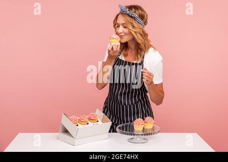 Blonde junge Erwachsene Bäcker nimmt Kuchen aus der Papierkiste, Vorbereitung für das Servieren für die Gäste, genießen von duftenden leckeren Dessert mit geschlossenen Augen. Innen Stockfoto