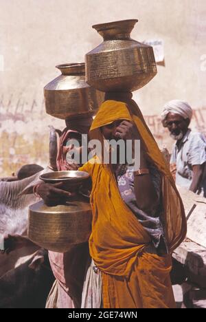 Indien. Rajasthan. Bundi. Einheimische Frauen tragen Messingwassergläser auf ihren Köpfen. Stockfoto