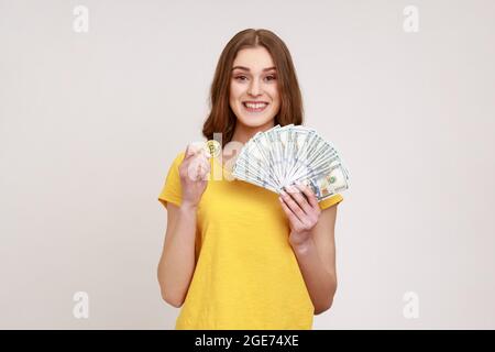 Attraktive glückliche Teenager-Mädchen in den Händen halten und zeigen Dollarscheine und goldene Münze der Krypto-Währung, Geld in digitale Bitcoins zu übertragen. Stockfoto