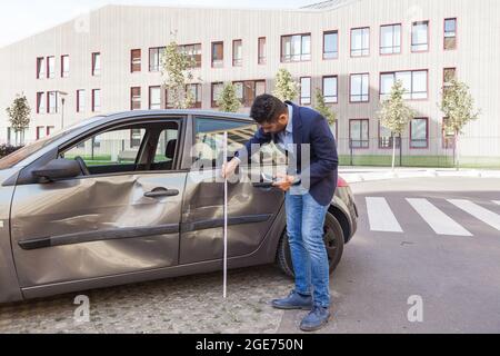 Versicherungsvertreter, der Jeans und Jacke trägt, schätzt den Autoschaden ein, beurteilt den Schaden am Automobil, Dellen und Kratzer an den Fahrzeugtüren nach der Abseinung Stockfoto