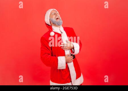 Porträt eines älteren Mannes mit grauem Bart, der das weihnachtsmann-Kostüm trägt und die Hände am Bauch hält, kann nicht aufhören, hart zu lachen, lustige Geschichten zu hören, Witz. Stockfoto