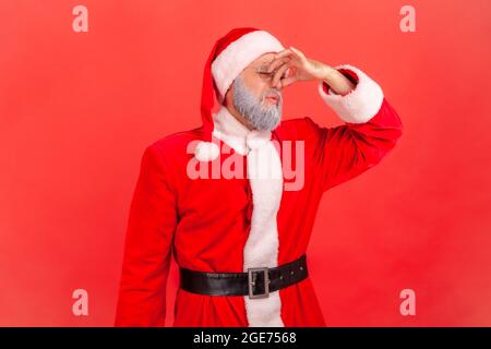 Porträt eines älteren Mannes mit grauem Bart im weihnachtsmann-Kostüm, der sich schrecklich übel gerochen fühlt, die Finger auf der Nase hält, widerlicher Ausdruck. Indoor st Stockfoto