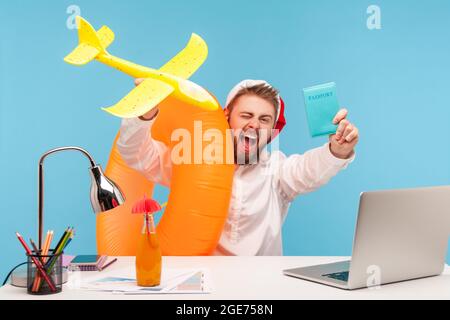 Extrem aufgeregt Mann in weihnachtsmann Hut gehen in den Winterferien, sitzen im Büro mit Gummiring und Spielzeug Flugzeug und zeigen Pass, Kauf Tick Stockfoto