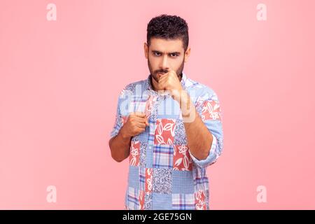 Porträt eines seriös schönen bärtigen Mannes im blauen Casual-Style-Shirt, der in Boxfäusten steht, die Kamera anschaut und bereit ist, anzugreifen oder zu verteidigen. Innen Stockfoto