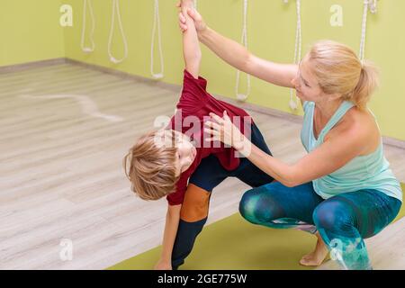 Eine Ausbilderin in einer Sportuniform ist mit einem Jungen im Yoga beschäftigt. Das Mädchen korrigiert die Asanas für das Kind. Ruhe, Balance und Konzentration konz Stockfoto