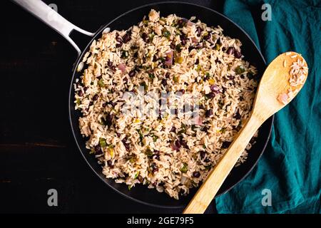 Koriander-Limettenreis mit schwarzen Bohnen in einer Pfanne: Eine Pfanne mit Bohnen und Reis mit Koriander, dargestellt mit einem Holzlöffel und einer Stoffserviette Stockfoto