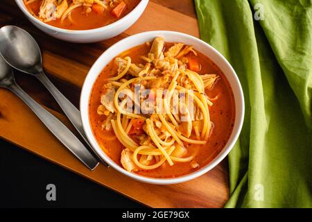 Kubanische Hühnernudelsuppe garniert mit Cilantro: Schalen mit Hühnernudelsuppe in einer Tomatenbrühe Stockfoto