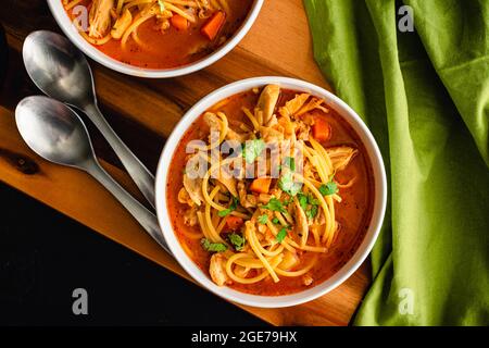 Kubanische Hühnernudelsuppe garniert mit Cilantro: Schalen mit Hühnernudelsuppe in einer Tomatenbrühe Stockfoto