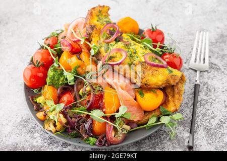 Omelette mit geschmortem Gemüse und Lachs, Tomaten mit Zwiebeln, Brokkoli und rotem Fisch mit Erbsen-Microgreens, leckeres herzhaftes Frühstück Stockfoto