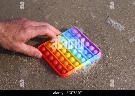 Das Anti-Stress-Pop-IT-Spielzeug liegt auf dem nassen Sand an der Küste. Stockfoto