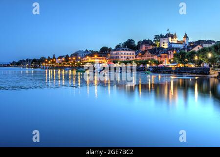 Sonnenuntergang über der bezaubernden Stadt Nyon am Ufer des Genfersees, Schweiz, mit dem mittelalterlichen weißen Schloss, das die Szene überragt. Stockfoto