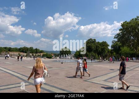 NIS, Serbien - 14. August 2021 großer Stadtplatz mit gepflastertem Boden und Brunnen, Menschen gehen an einem heißen sonnigen Sommertag in der Stadt Nis Stockfoto