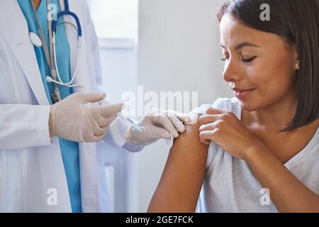 Junge glückliche afro-amerikanische Patientin, die in der Klinik eine Injektion des Coronavirus-Impfstoffs erhalten hat Stockfoto