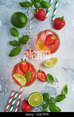 Zwei Gläser Punsch und frische Zutaten für die Herstellung von Limonade, infusem Detox-Wasser oder Cocktail. Erdbeeren, Limette, Minze, Basilikum, Eiswürfel und Shaker Stockfoto