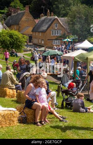 Großbritannien, England, Oxfordshire, Wroxton, jährliches Kirchenfest im Gange, Besucher entspannen sich im Sommersonne auf dem Dorfgrün Stockfoto