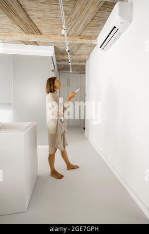Frau stellt die Temperatur an der Klimaanlage zu Hause ein Stockfoto