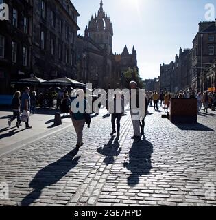 Royal Mile, Edinburgh, Schottland, UK Wetter. August 2021. Sonniger Abend auf der gepflasterten High Street mit Silhouetten umherschwirrenden Menschen, die auf der Suche nach Unterhaltung von den letzten Shows des Tages von Straßenunterhaltern sind. Quelle: Arch White/Alamy Live News Stockfoto