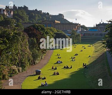 Edinburgh, Schottland, Vereinigtes Königreich Wetter. August 2021. Sonniger Abend im Princes Street Gardens East mit Leuten, die auf dem Gras sitzen und das Edinburgh Castle im Hintergrund bewundern. Quelle: Arch White/Alamy Live News. Stockfoto