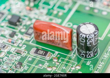 Nahaufnahme eines orangefarbenen eingetauchten Polyesterfolienkondensators auf der grünen leiterplatte. Für bedrahteten Kondensator, kleine elektronische Bauteile. Hersteller nicht identifiziert Stockfoto