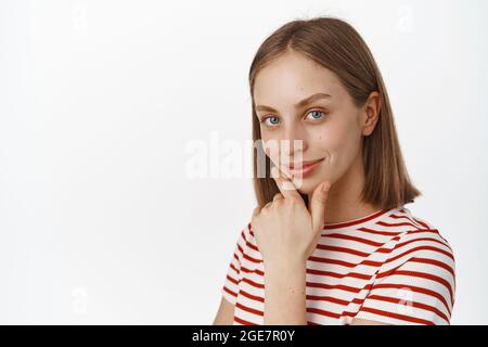 Nahaufnahme Porträt der schönen jungen Frau mit blonden Haaren, blauen Augen und natürlich leuchtende Haut ohne Make-up, sauberes Gesicht, berühren Kinn und aussehen Stockfoto