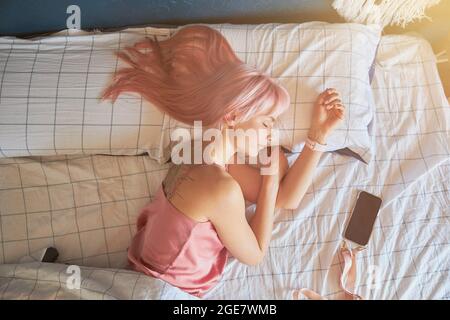 Frau mit rosafarbenen Haaren und großem Tattoo auf dem Rücken schläft in einem bequemen Bett Stockfoto
