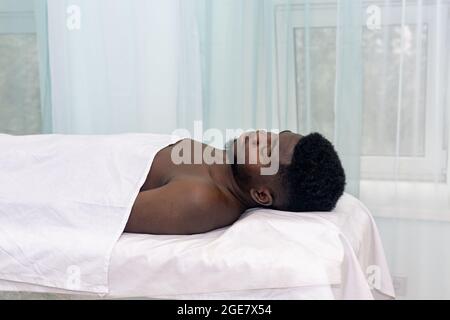 Schwarzer Mann liegt mit geschlossenen Augen auf einem Bett in einer medizinischen Einrichtung Stockfoto