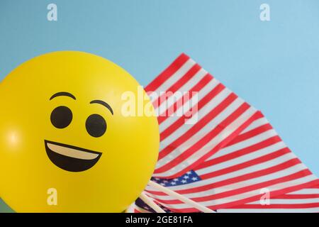 Gelbe Emoji-Ballons mit amerikanischen Flaggen auf blauem Hintergrund. Stockfoto