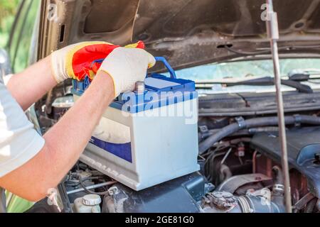 Wartung der Maschine. Ein männlicher Automechaniker nimmt eine Batterie unter der Motorhaube eines Autos heraus, um sie zu reparieren, aufzuladen oder zu ersetzen. Stockfoto