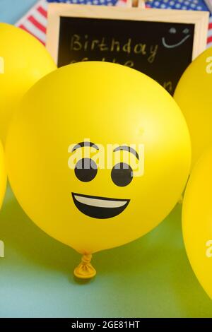 Gelbe Emoji-Ballons auf dem Hintergrund der Tafel mit der Ereignisbeschriftung und amerikanischen Flaggen. Stockfoto