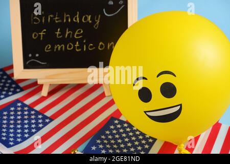 Gelbe Emoji-Ballons auf dem Hintergrund der Tafel mit der Ereignisbeschriftung und amerikanischen Flaggen. Stockfoto