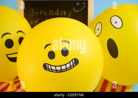 Gelbe Emoji-Ballons auf dem Hintergrund der Tafel mit der Ereignisbeschriftung und amerikanischen Flaggen. Stockfoto