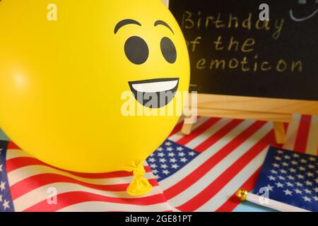 Gelbe Emoji-Ballons auf dem Hintergrund der Tafel mit der Ereignisbeschriftung und amerikanischen Flaggen. Stockfoto