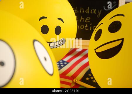 Gelbe Emoji-Ballons auf dem Hintergrund der Tafel mit der Ereignisbeschriftung und amerikanischen Flaggen. Stockfoto