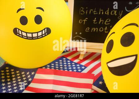 Gelbe Emoji-Ballons auf dem Hintergrund der Tafel mit der Ereignisbeschriftung und amerikanischen Flaggen. Stockfoto