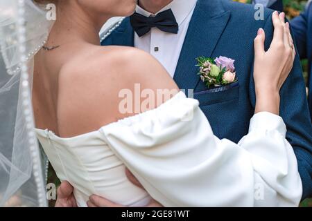 Der Bräutigam in einem blauen Anzug und die Braut in einem weißen Kleid umarmen sich. Die Hand einer Frau mit einem Ring auf der Schulter eines Mannes. Hochzeit, Verlobung. Liebe und Liebe Stockfoto