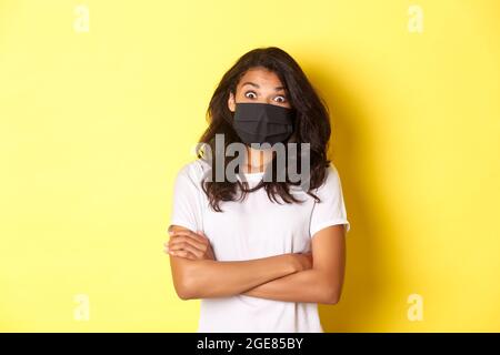 Konzept von Coronavirus, Pandemie und Lebensstil. Bild von überrascht afroamerikanischen Mädchen in Gesichtsmaske, Blick erstaunt auf etwas cool, stehen über Stockfoto