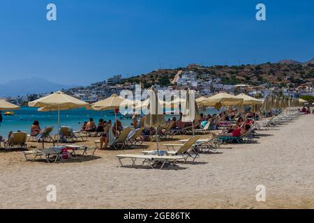 ELOUNDA, KRETA - 11. JULI 2021: Touristen am öffentlichen Strand in der Stadt Elounda auf Kreta, Griechenland Stockfoto