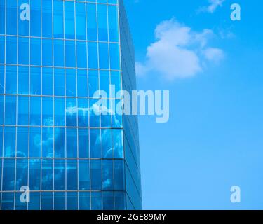 Modernes Business-Bürogebäude aus Glas mit blauem Himmel und Wolken im Spiegelbild der Fenster Stockfoto