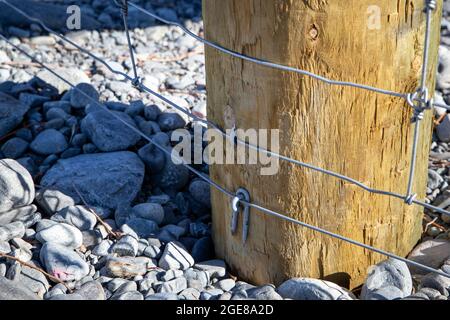 Nahaufnahme von Komponenten eines Pfostens und eines Gitterzauns entlang der Grenze zwischen dem Hof und dem Flussbett, Canterbury, Neuseeland Stockfoto