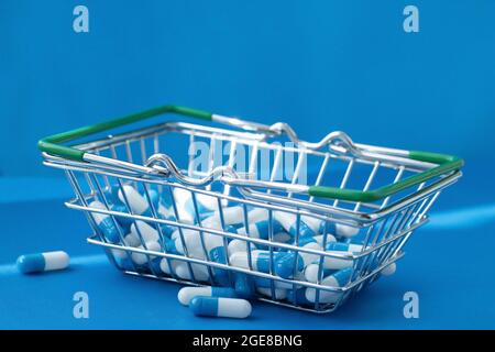 Pillen in einem Lebensmittelkorb. Medikamentenkapseln auf dem Tisch. Käufer in der Apotheke. Medikamente online bestellen. Pillen auf blauem Hintergrund in einer Schachtel. Stockfoto