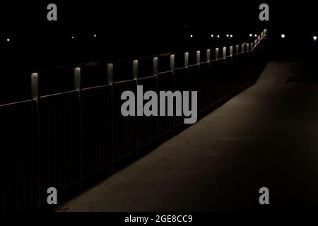 Parkweg bei Nacht. Das Licht der Fanaren auf der Uferbrücke. Weg im Dunkeln. Platz für einen Spaziergang. Stockfoto