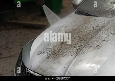 Autowäsche. Das Auto wird unter dem Druck eines Wasserstrahls gewaschen. Mit einem Wasserspray Schmutz von der Fahrzeugoberfläche abwaschen. Stockfoto